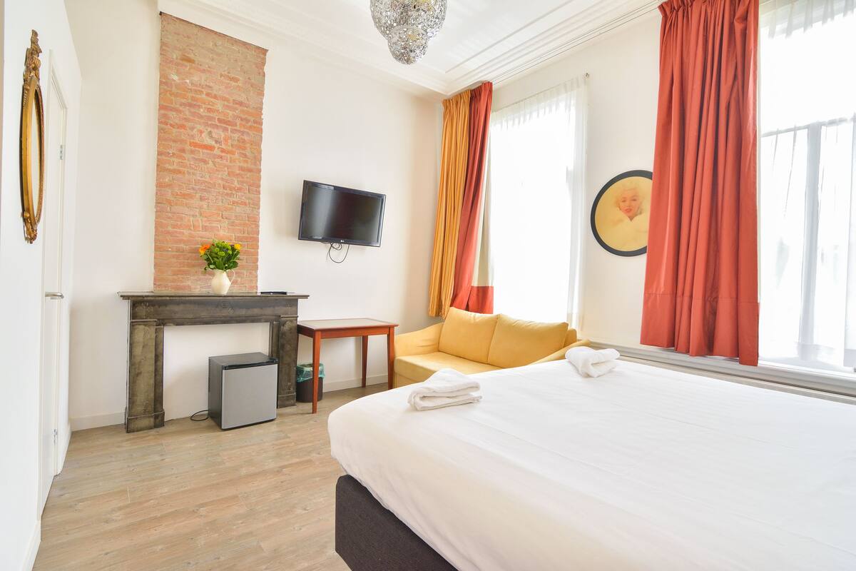 Habitación de hotel con cama, televisor, una mesita, sofá y pared de ladrillo.