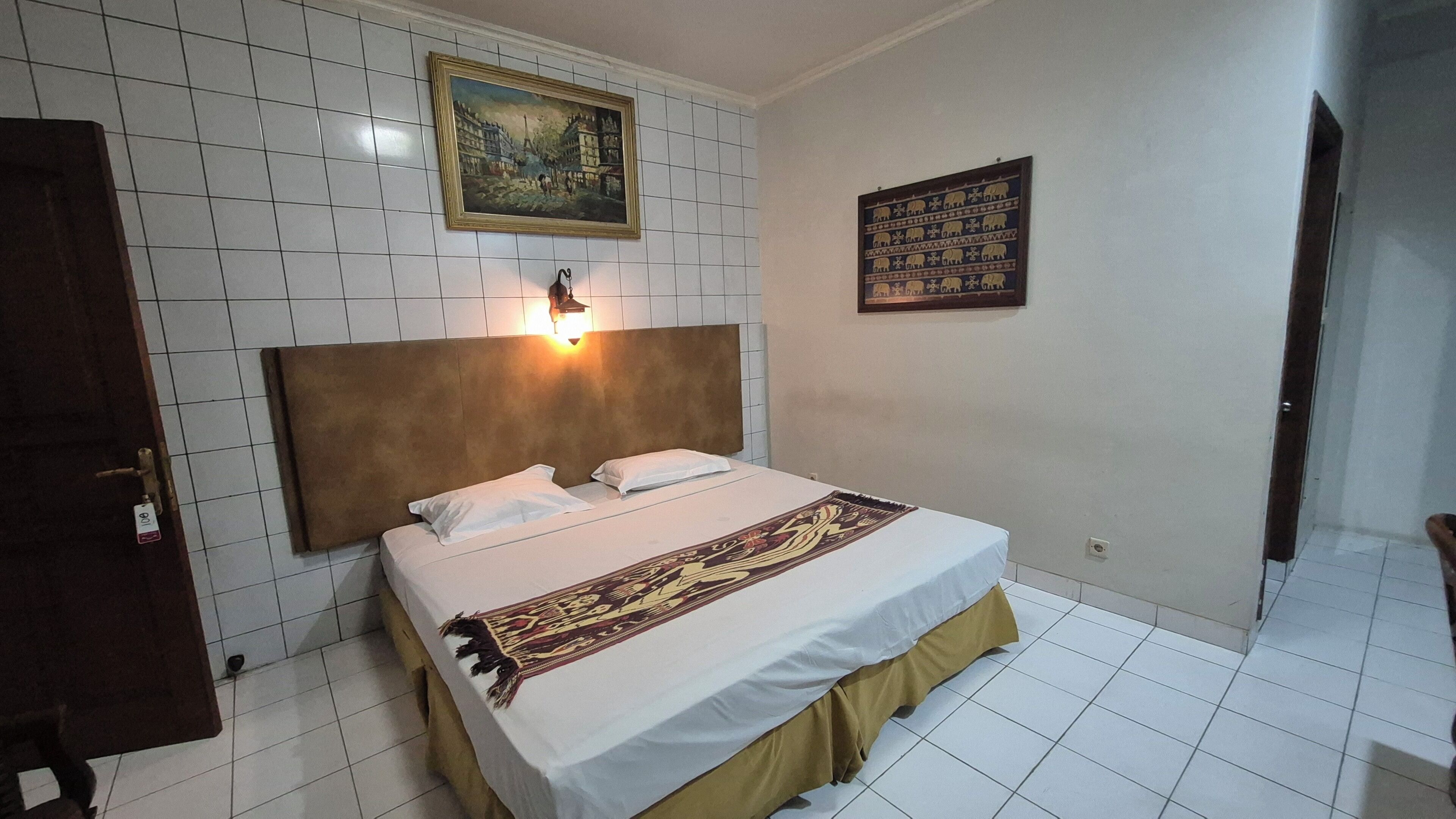 A hotel room with a bed, a headboard, a painting, and a wall-mounted decorative item.