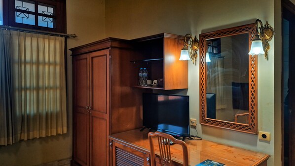 Una habitación con escritorio de madera, televisor, armario y espejo con luces empotradas.