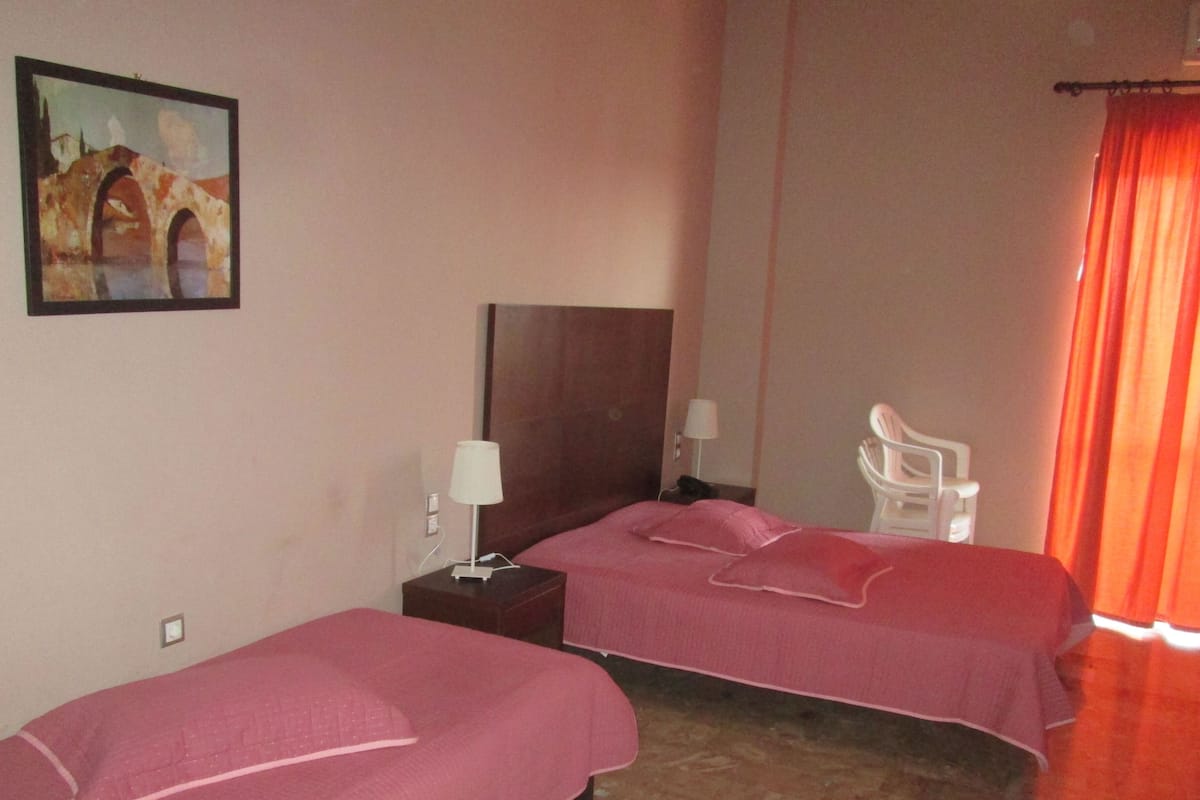 A hotel room with two beds, a nightstand, a lamp, a chair, and a painting on the wall.