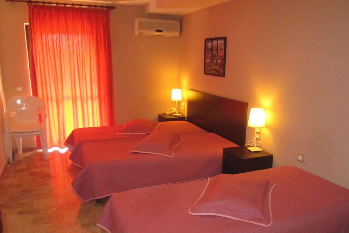 A hotel room with two beds, a chair, a nightstand with a lamp, and a painting on the wall.