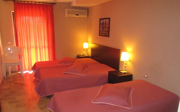 A hotel room with two beds, a chair, a nightstand with a lamp, and a painting on the wall. - Vanisko Hotel (Malevizi)