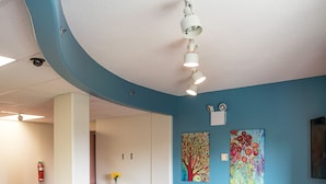 A modern lounge area with a curved ceiling, a green sofa, a blue sofa, and a small table with a vase of flowers. - Mount Saint Vincent University Residence - Hostel (Halifax)