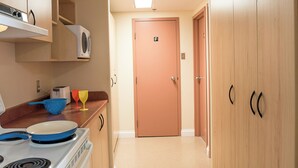 A narrow kitchen with wooden cabinets, a stove, and a microwave. - Mount Saint Vincent University Residence - Hostel (Halifax)