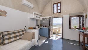 A cozy room with a kitchenette, a sofa with a checkered blanket, and a view of the landscape through a window.