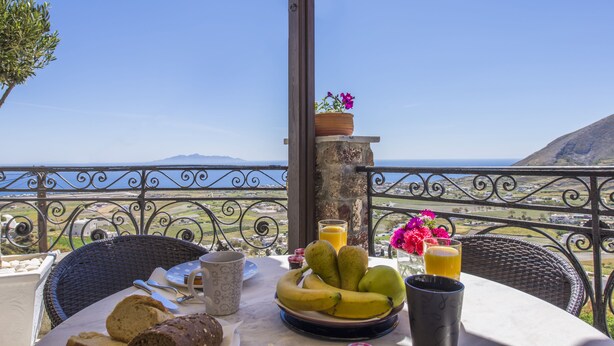 A table with breakfast items, a view of the sea, and a mountain in the background.