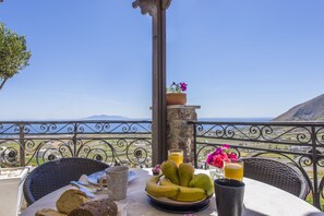 Una mesa con alimentos para el desayuno, vista al mar y una montaña al fondo.