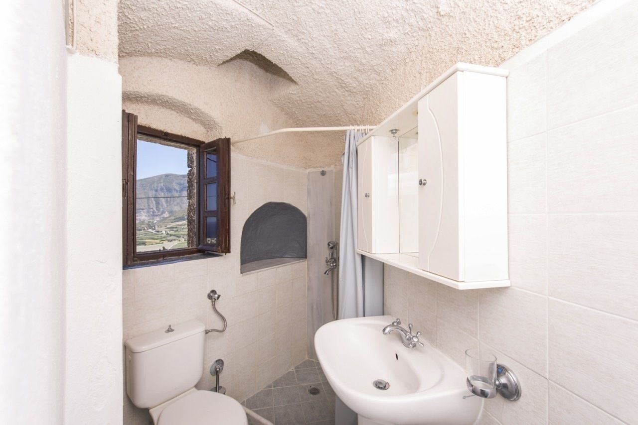 Un baño pequeño con inodoro, lavamanos y ducha. Se ve una ventana con vistas a montañas.