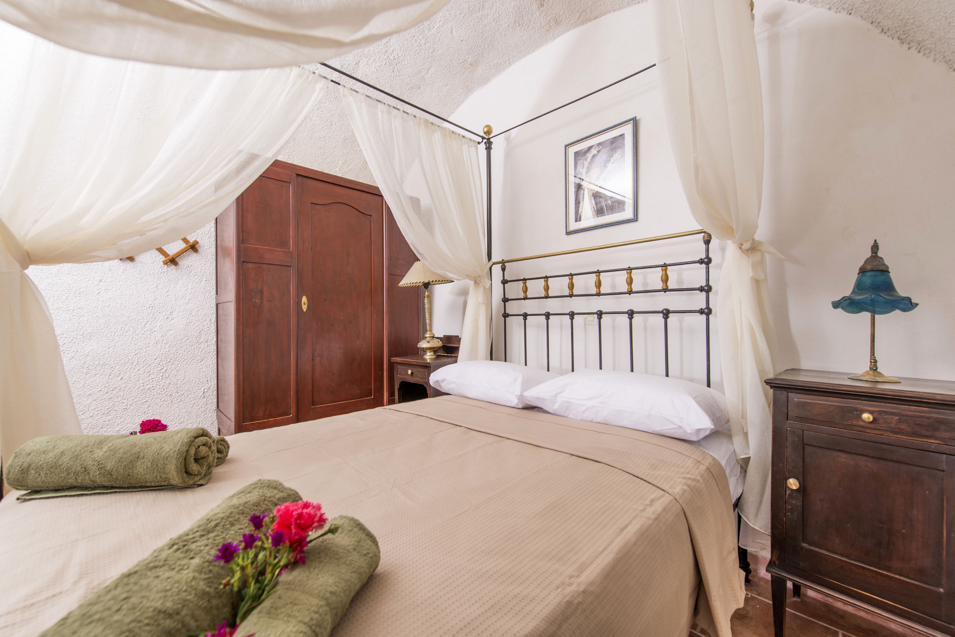 A neatly made bed with a white headboard, a wooden nightstand with a lamp, and a wooden wardrobe.