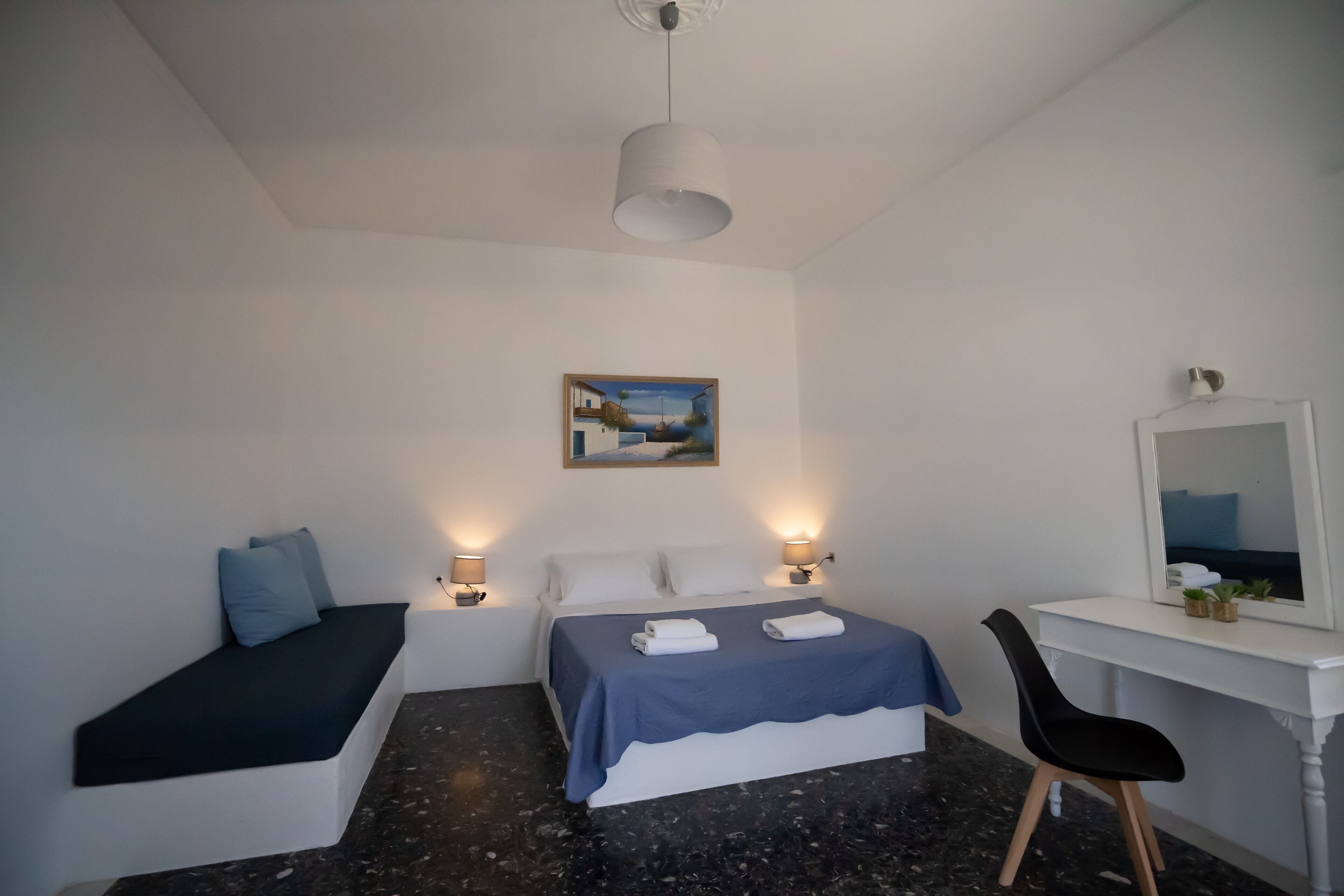 A bedroom with a bed, bedside lamps, a desk with a mirror, and a painting on the wall.