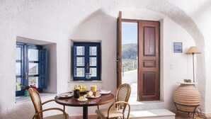 A dining area with a round table, wicker chairs, and a view of the countryside through an open door.