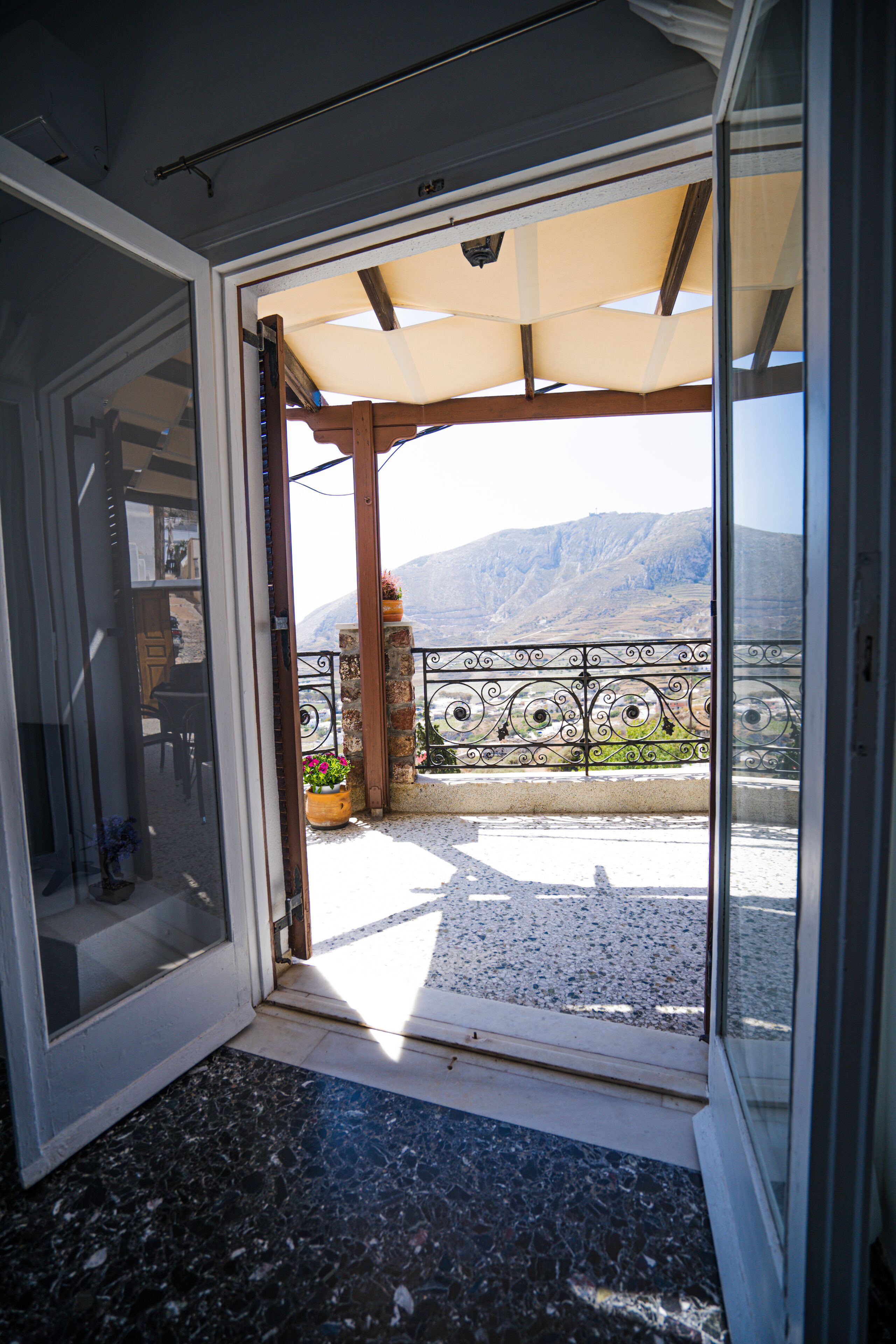 Un balcon avec vue sur les montagnes, une pergola et un pilier en pierre surmonté d’un pot de fleurs.