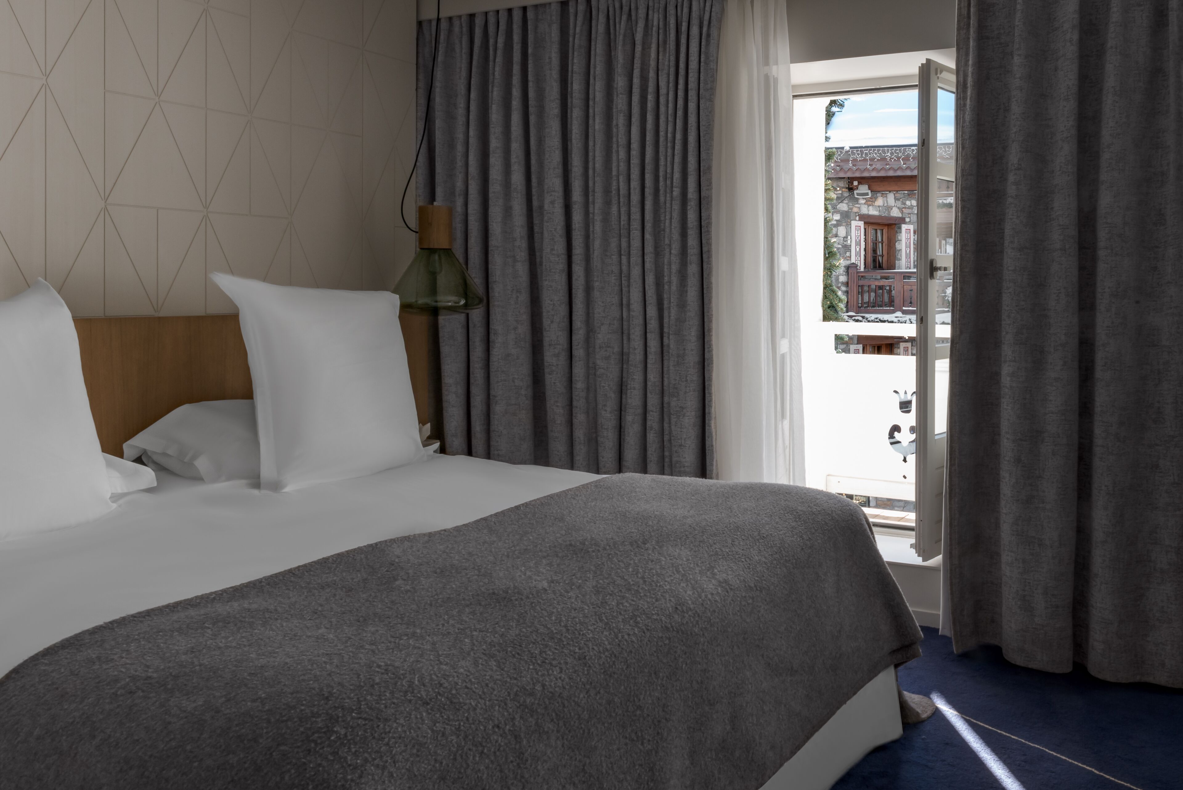 A hotel room with a large bed, grey curtains, and a view of a building outside.