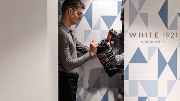 Un hombre observa un par de zapatos frente a una pared con diseños geométricos y la leyenda "WHITE 1921 COURCHEVEL".