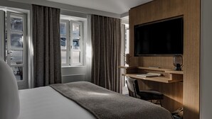 A modern hotel room with a large bed, a desk with a computer, a flat-screen TV, and a window with curtains. - White 1921 Courchevel (Courchevel)