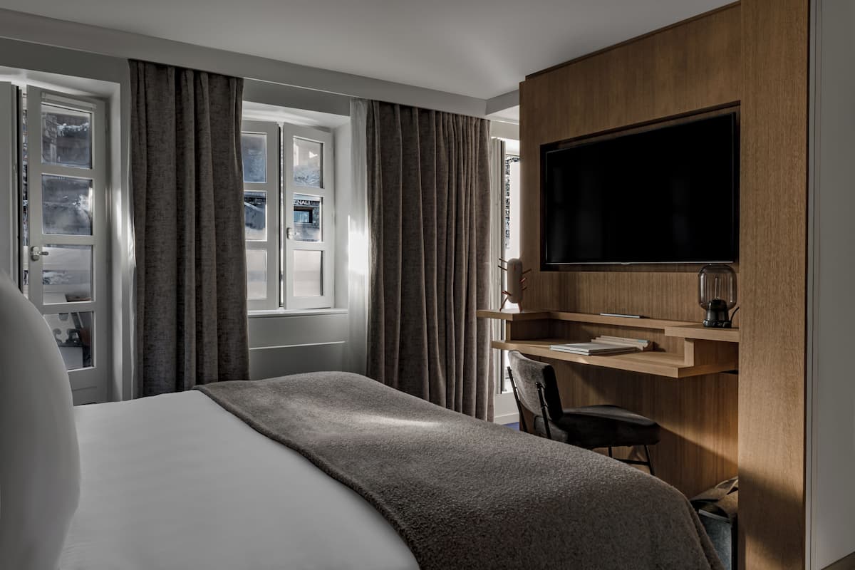 A modern hotel room with a large bed, a desk with a computer, a flat-screen TV, and a window with curtains.