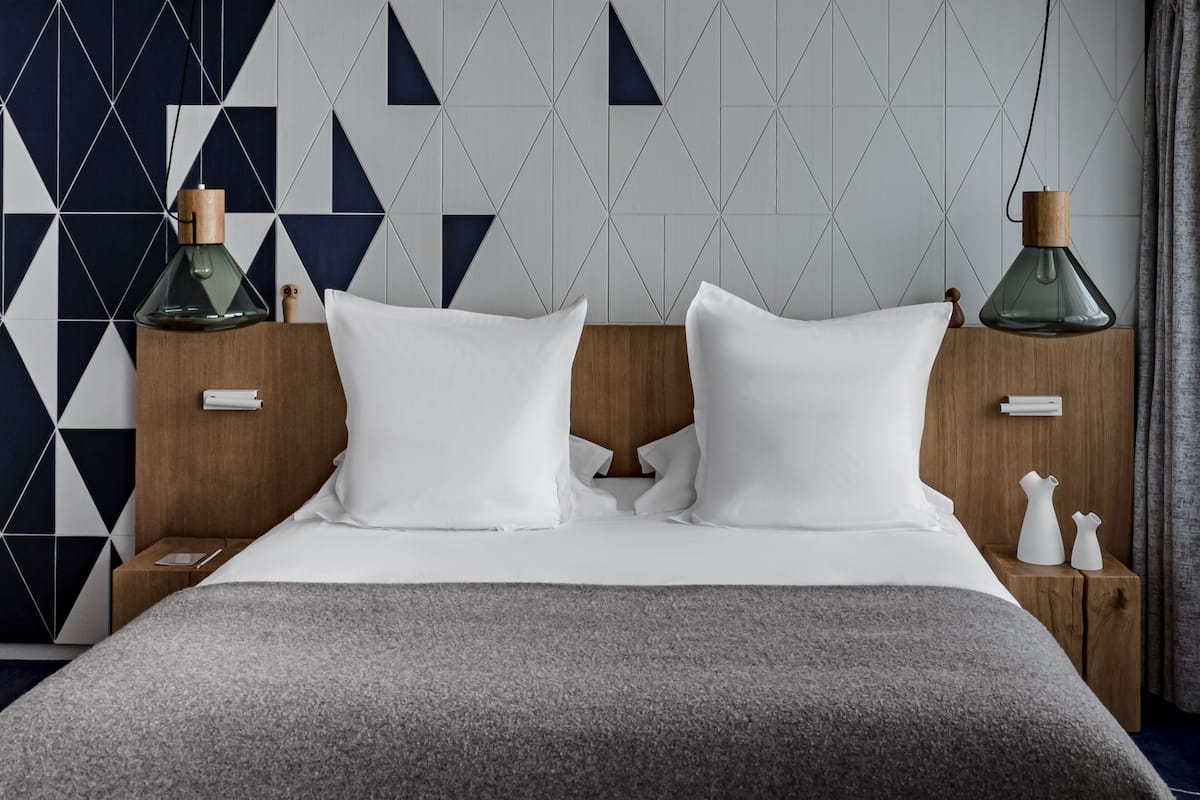 A neatly made bed with white linens, a grey throw blanket, and two bedside tables with decorative vases.