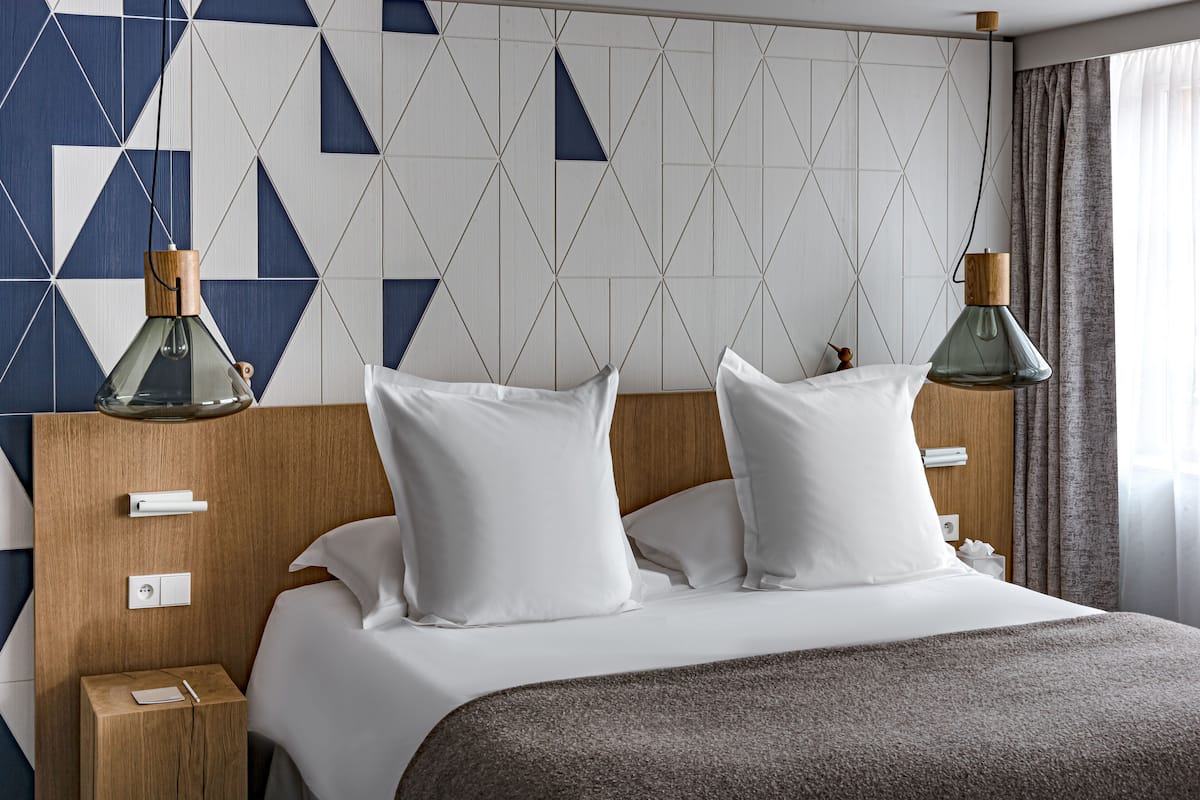 A neatly made bed with white bedding and pillows, a wooden headboard, and two bedside tables with lamps.