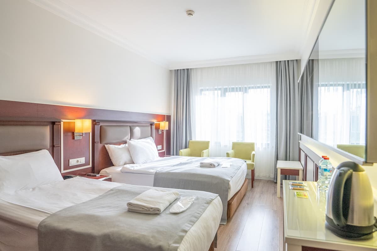 A hotel room with two beds, a desk, a chair, and a large window with curtains.