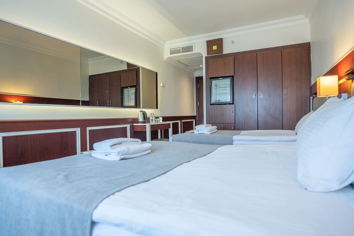 A hotel room with two beds, a large mirror, a wooden wardrobe, and a small table with toiletries.