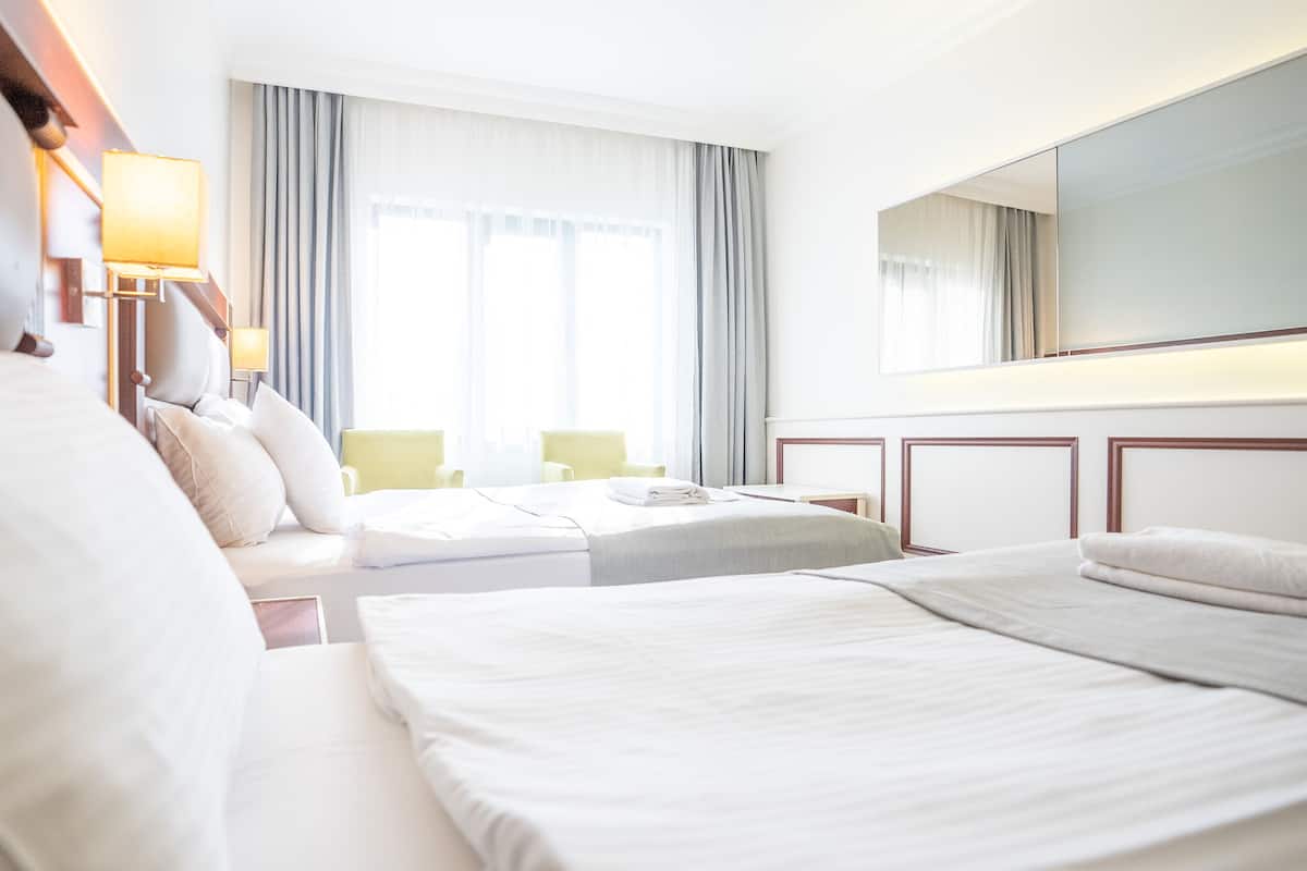 A hotel room with two beds, a sofa, a chair, a desk, and a large mirror.