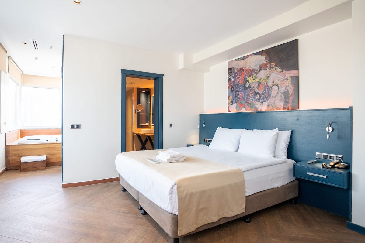 A hotel room with a bed, bedside table, and a painting on the wall.