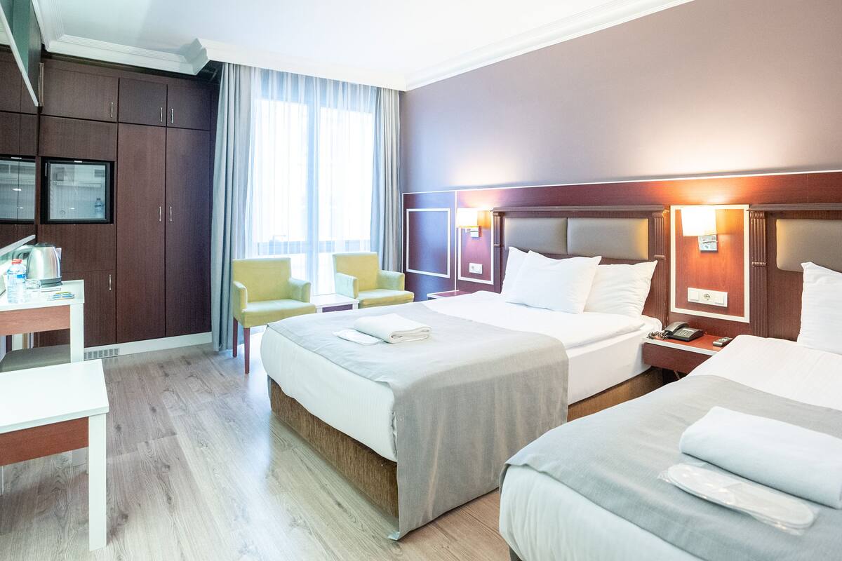 A hotel room with two beds, a desk, a chair, and a television.
