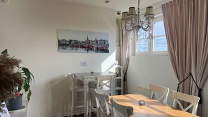 A dining area with a table and chairs, a chandelier, a painting on the wall, and a window with curtains. - Crafoord Place - Hostel (Stockholm)