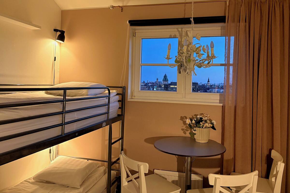 A bunk bed room with a city view, a chandelier, a table with chairs, and a window with curtains.