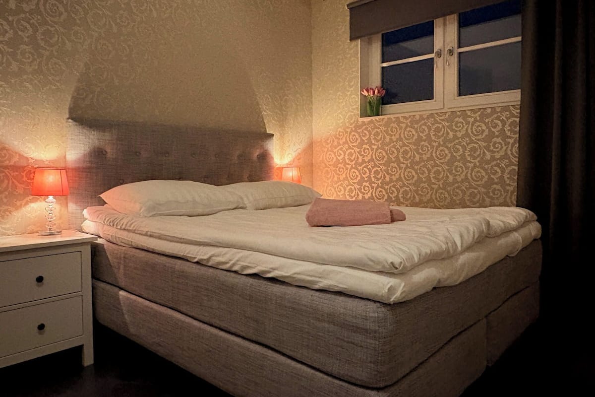 A neatly made bed with a pillow, a bedside lamp, and a window with a view of the outside.