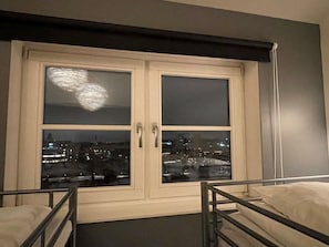 A room with a bed, a window with a view of a cityscape, and a door with a handle.