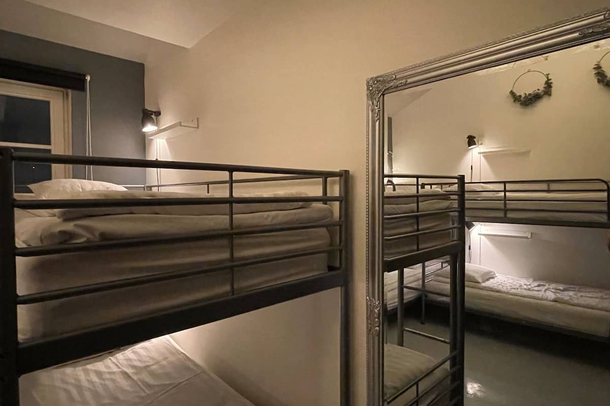 Bunk beds in a room with a mirror reflecting the bed and a wall-mounted light fixture.
