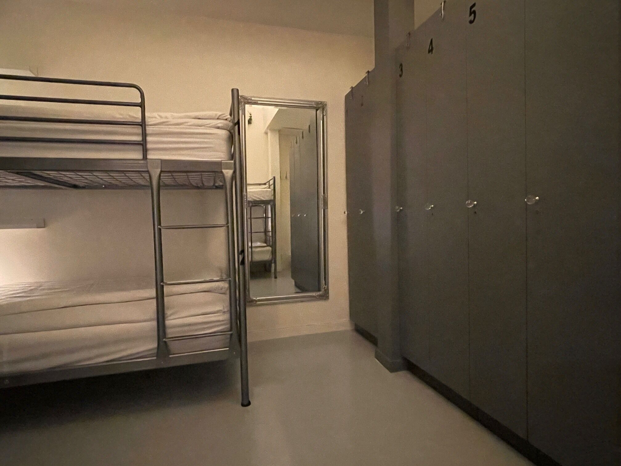 Una cama litera con escalera, un espejo y un armario con puertas numeradas.