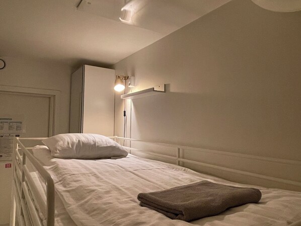 A single bed with white bedding, a brown towel, and a wall-mounted light fixture.