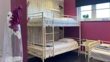 A bunk bed room with a window, a small table with a plant, and a vase of flowers.