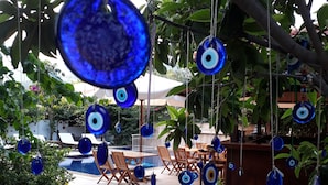 A poolside area with blue decorative hanging items, wooden lounge chairs, and a pool. - Kybele Hotel (Fethiye)