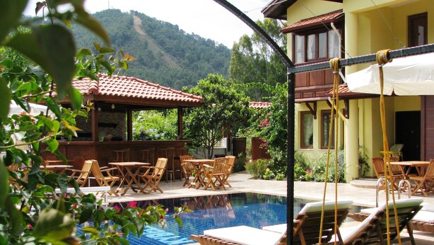 A pool area with lounge chairs, a bar, and a view of the mountains. - Kybele Hotel (Fethiye)