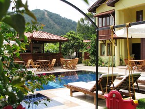 A pool area with lounge chairs, a bar, and a view of the mountains. - Kybele Hotel (Fethiye)