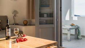 Una habitación con una mesa de madera, una botella de vino y una copa de vino. Hay un cuenco de tomates sobre la mesa.