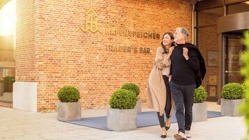A couple walking in front of a building with a brick facade and a sign that reads "Hotel Hafenspeicher Trader's Bar."