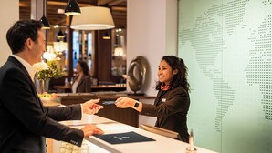 A hotel reception area with a modern design, including a reception desk, a globe wall, and a vase with flowers. - Hotel Hafenspeicher (Leer)