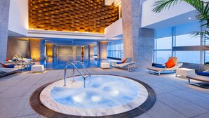 Zona d'una piscina interior moderna amb banyera hidromassatge, gandules i vistes a la ciutat.