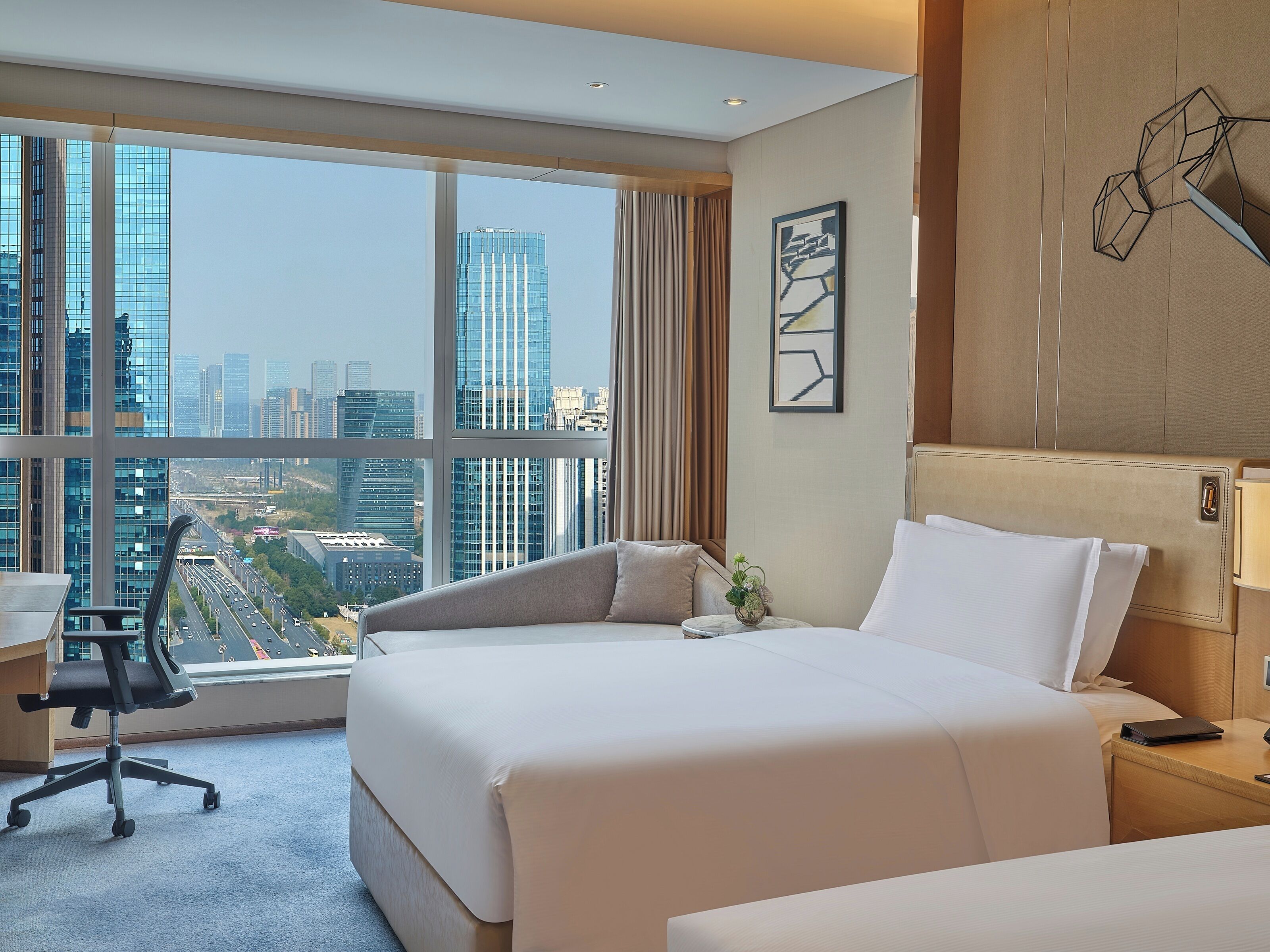 A hotel room with a large bed, a desk, and a view of a cityscape.