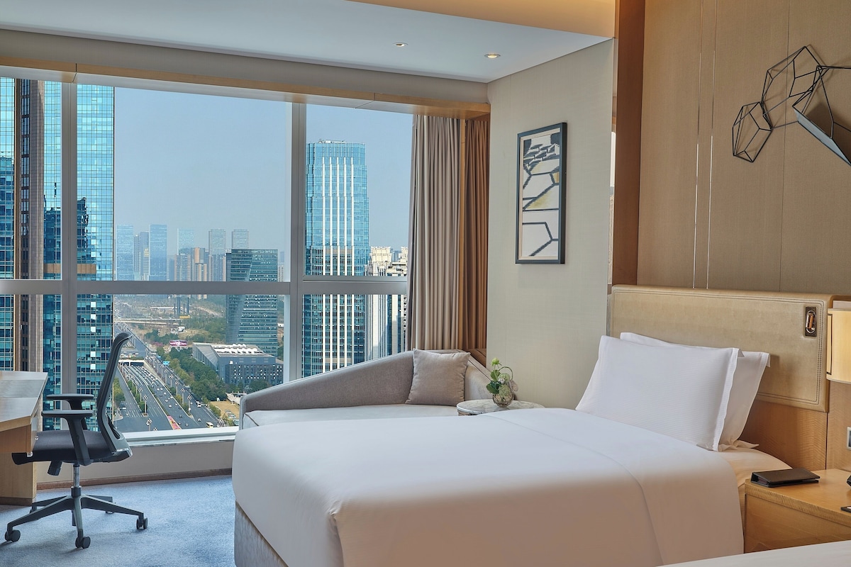 A hotel room with a large bed, a desk, and a view of a cityscape.