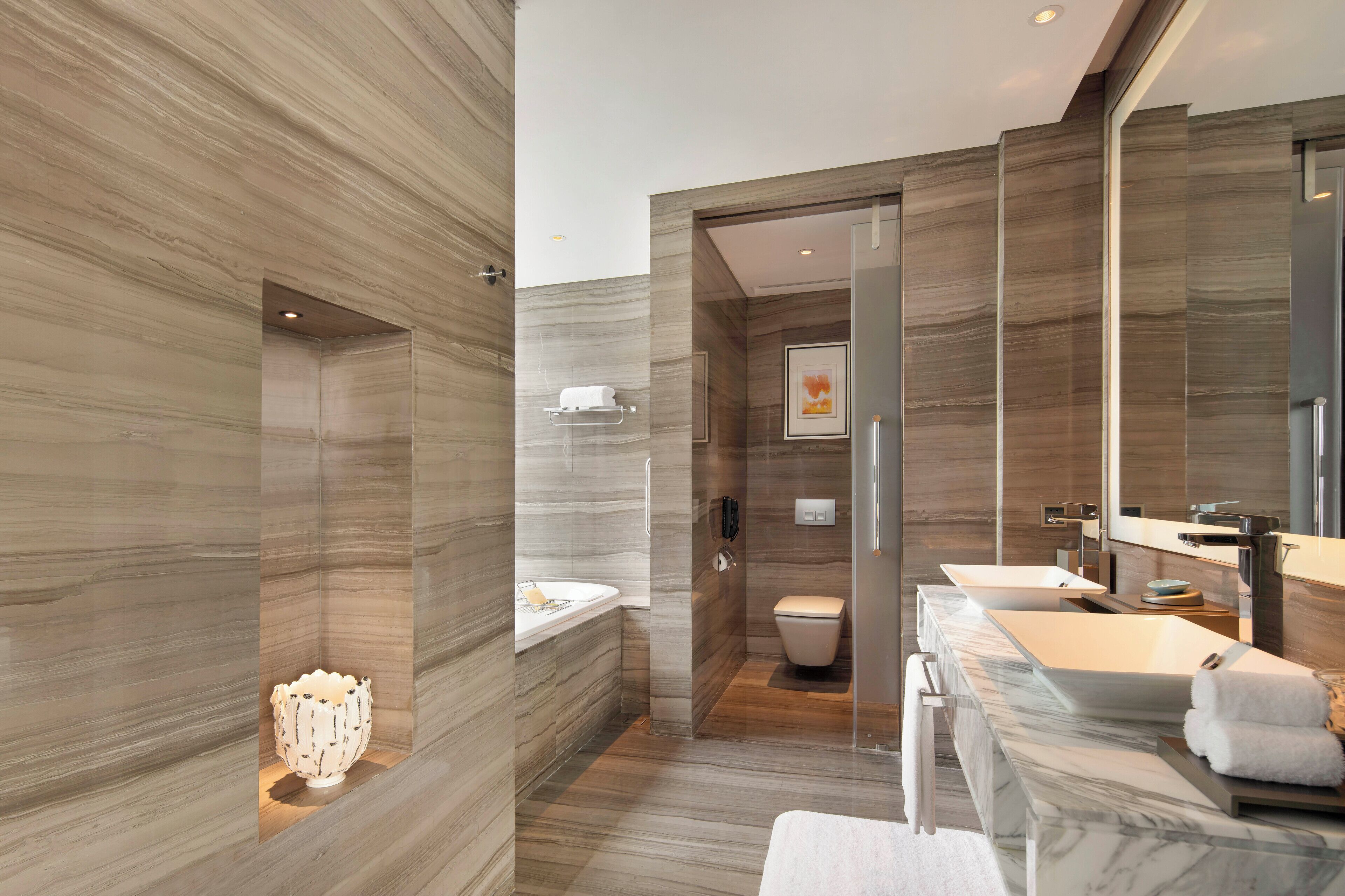 A modern bathroom with a marble vanity, a large mirror, and a separate toilet area.