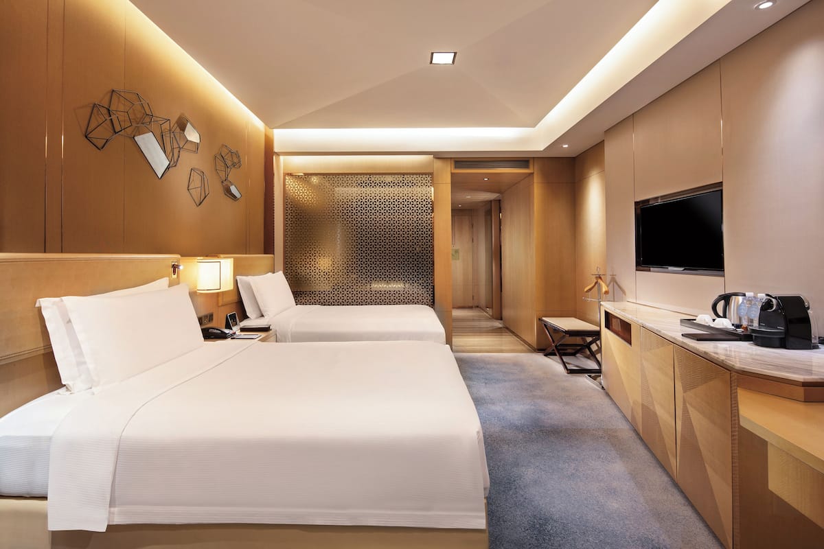 A hotel room with two beds, a desk with a flat-screen TV, a coffee maker, and a patterned wall.