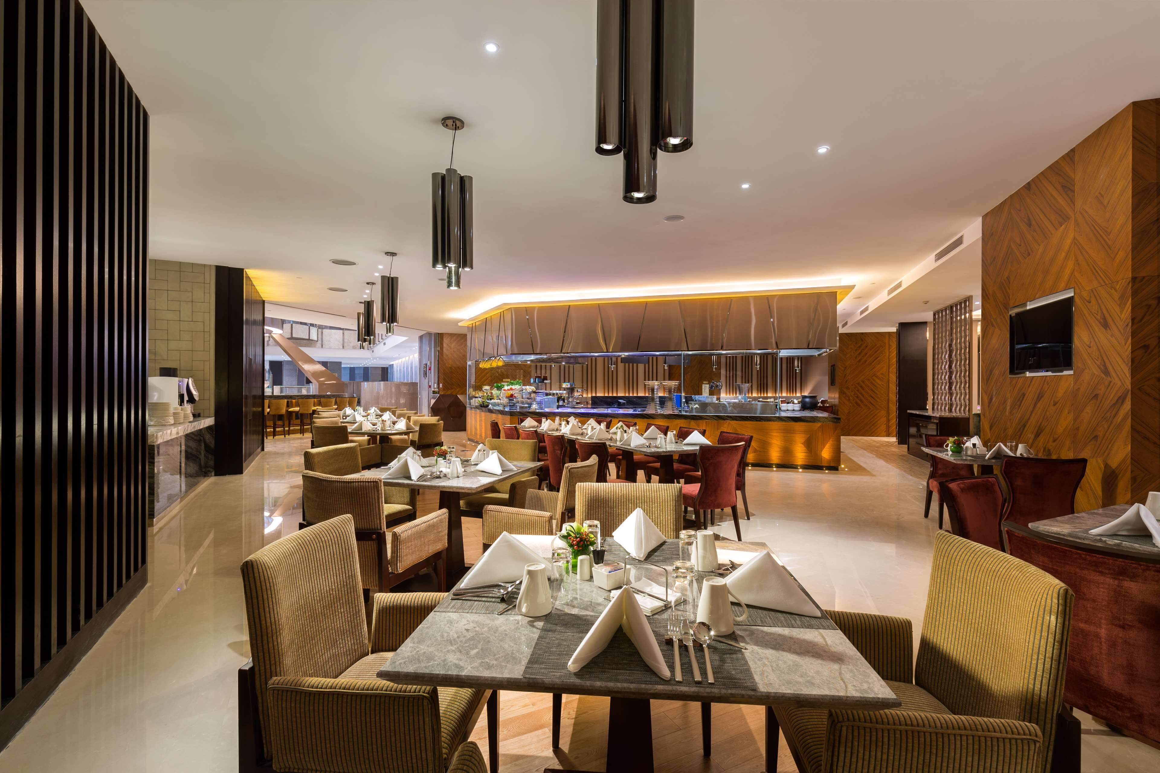 Een moderne hotelentree met een centraal gelegen bar, meerdere eettafels met stoelen en een gepolijste vloer.