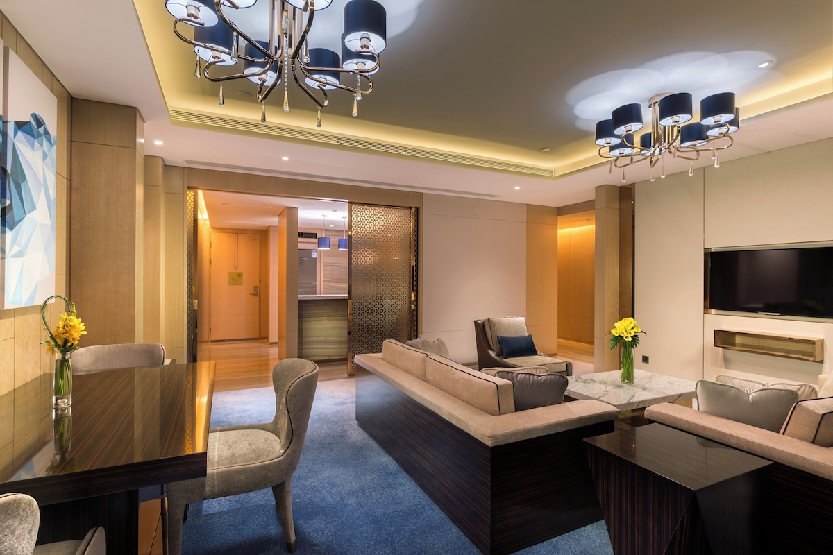 A modern hotel room with a dining area, sofa set, and a TV.