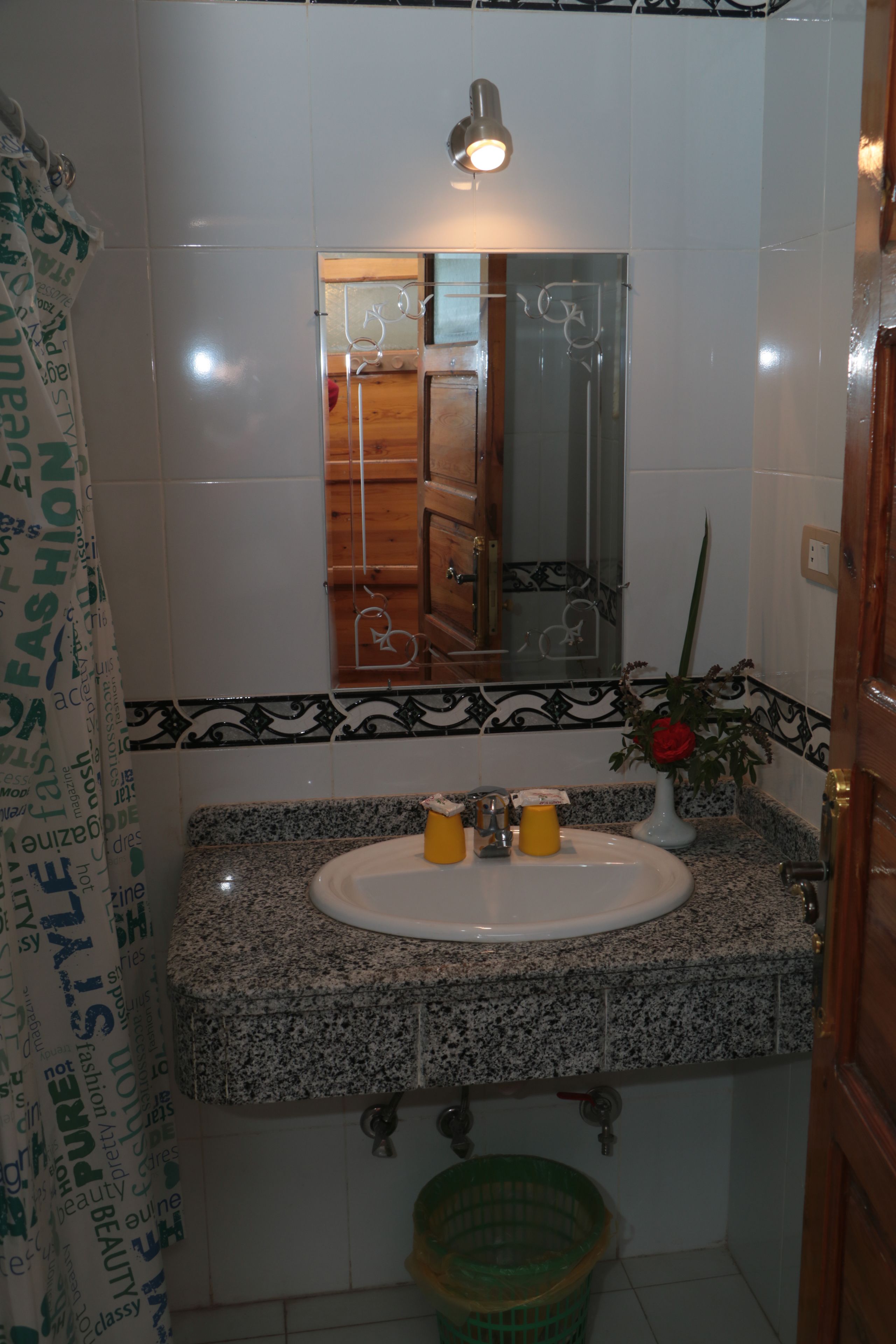 Baño con lavamanos de encimera de granito, espejo y cesta verde.
