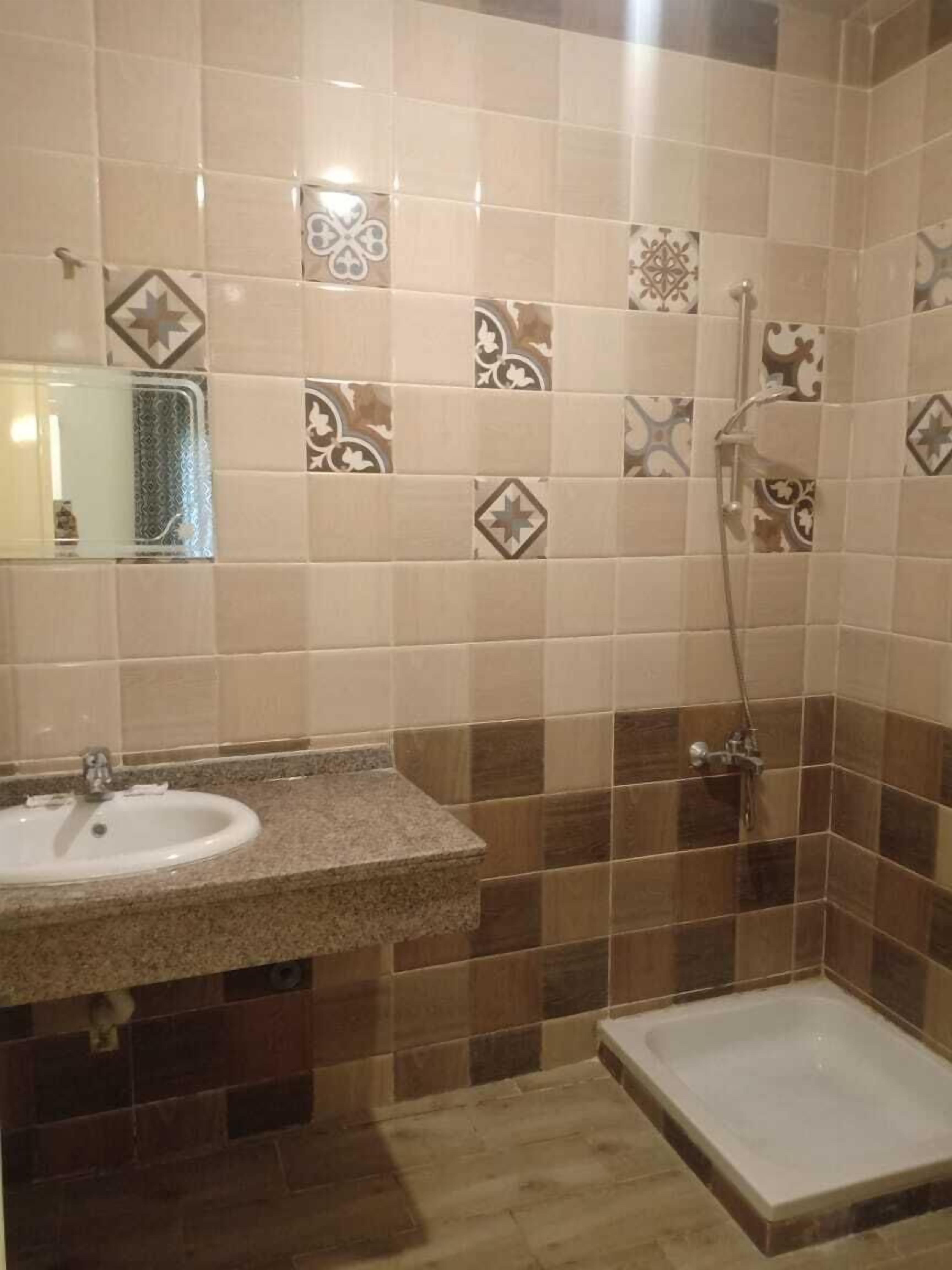 Un baño con lavamanos, espejo, ducha y paredes con azulejos.
